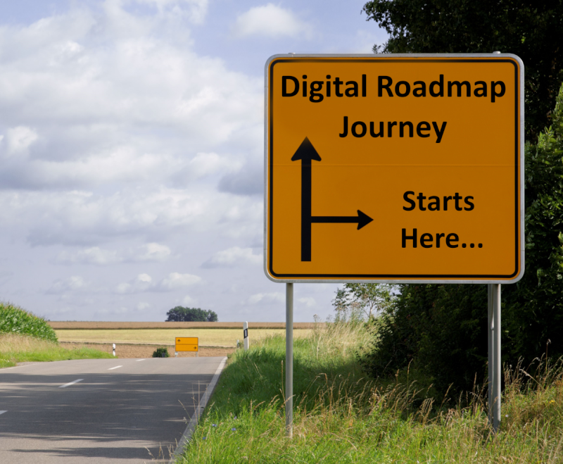 Photo of a road with grass verges and a large yellow sign that has the wording Digital Roadmap Journey Start Here.