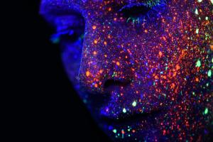 Face under UV light with glowing reflected multicoloured dots on it