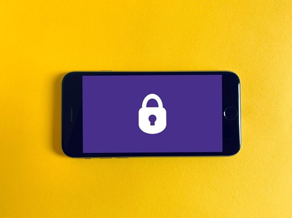 Mobile phone showing purple screen with white locked icon photographed agains a yellow background