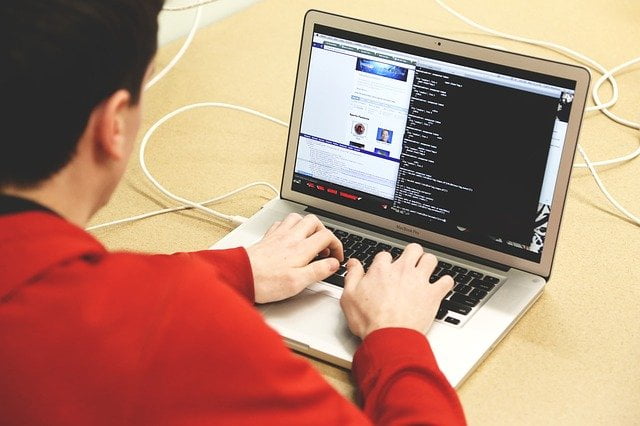 Software programmer types into laptop showing software code on screen