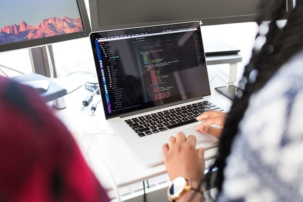 Software developer writes code into laptop on a desk
