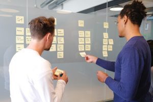 Product manager talks to product owner in front of a project planning board in an office