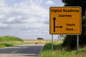 Road with grassy verges and large yellow square sign that Says Digital Roadmap Journey, Starts Here.