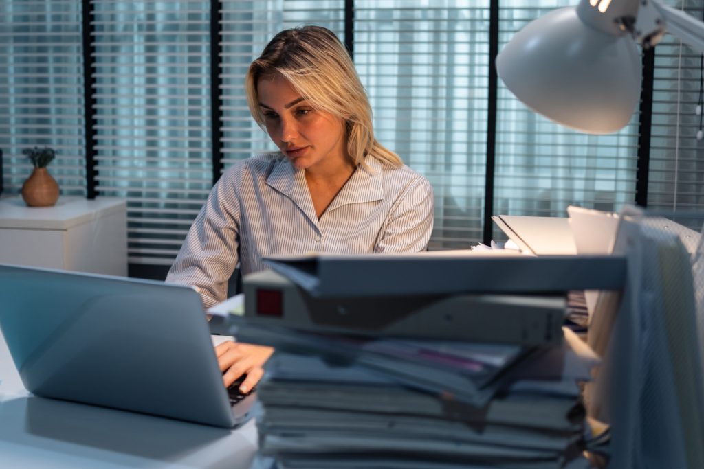 Lady working through the night due to mountains of paperwork, caused by using spreadsheets to manage a business. Custom software the solution to spreadsheet challenges.
