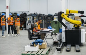 Photo of a factory with a man programming a robot to represent automation of systems.