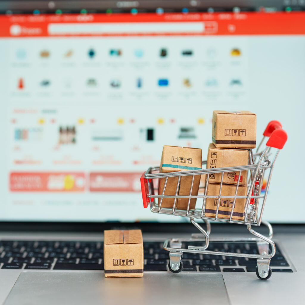 Photo showing a online store screen in the background and a mini trolley full of parcels in the foreground to represent online retail.