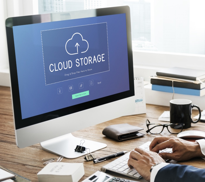 Photo of man and monitor, on the monitor screen is shown a cloud upward arrow and the working cloud storage.