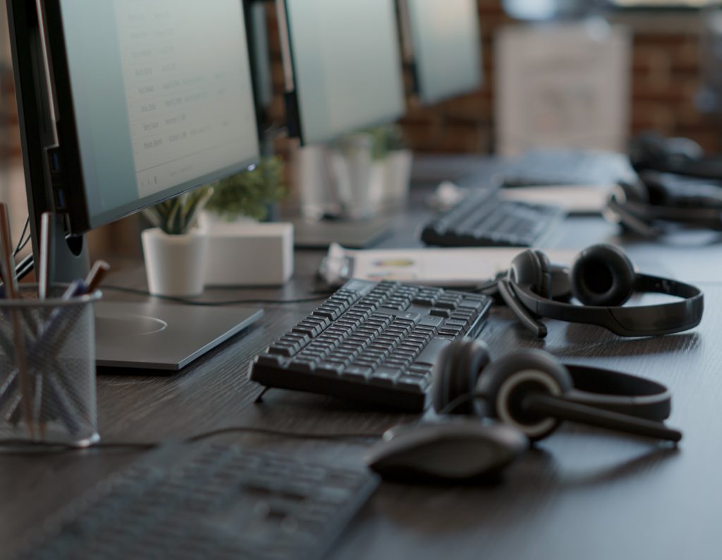 Photo of a long office desk with monitors and headphones shown in a row.