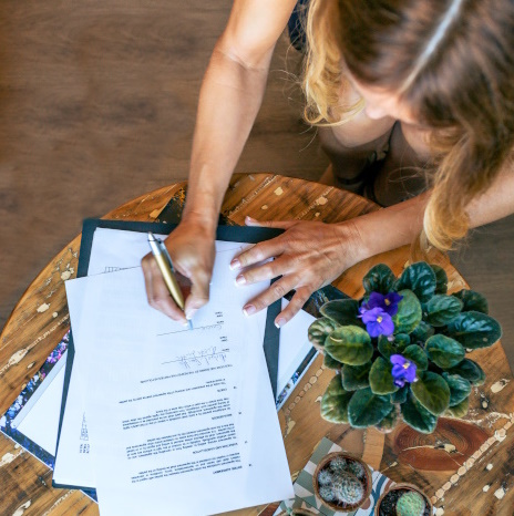 Photo a woman signing an SLA on a desk with plants to represent ensuring you avoid pitfalls before signing an SLA for any industry or SLA for software.