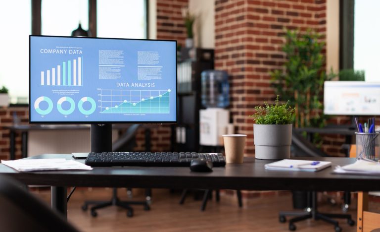 Photo of an office, desk, plant with a monitor and keyboard. The monitor is show reporting software.