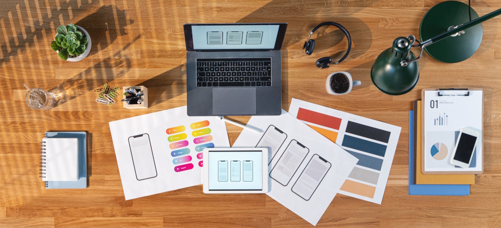 Table with laptop and paper showing screen layouts on a wooden desk.